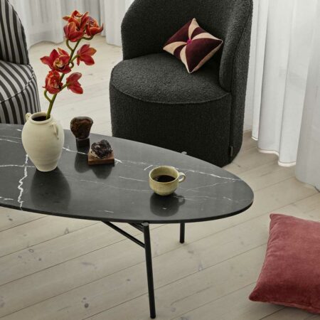 Scène représentant un salon avec parquet où se trouvent 1 fauteuil Lounge en tissu doux bouclé gris charbon et une table basse ovale en marbre noir.