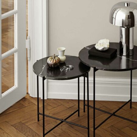 Tables gigognes rondes avec plateau en marbre noir et pied en métal noir. Une table est surmonté d'une lampe chromée. Parquet foncé à chevrons au sol