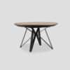 Table à manger extensible dotée d'un plateau rond en bois de chêne et d'un pied original et design, en métal noir composé de 4 épingles reliées en leur centre à un châssis métal rond qui soutient le plateau. La table est dotée de 2 rallonges en chêne.