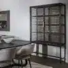 Salle à manger mettant en scène le buffet vitré en chêne foncé et la table à manger ovale ANDROMEDE également en chêne foncé avec chaises grises en velours.