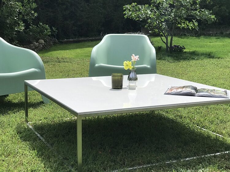 table basse de salon de jardin avec plateau en céramique blanche et piétement en inox au design fin, minimaliste et élégant. Deux fauteuils complètent l'ensemble.