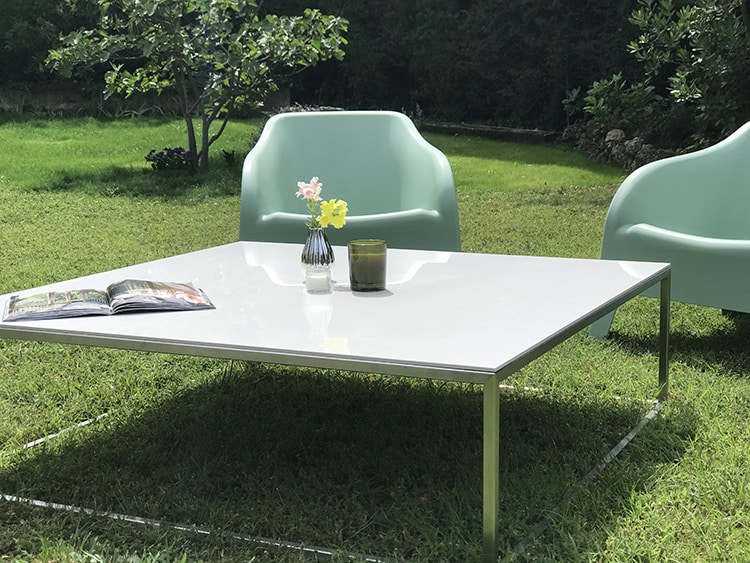 table basse de salon de jardin avec plateau en céramique blanche et piétement en inox au design fin, minimaliste et élégant. Deux fauteuils complètent l'ensemble.