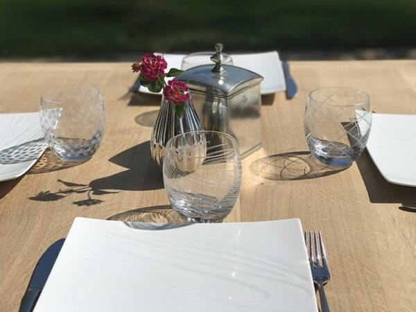 Détail du plateau carré en chêne massif naturel présenté avec assiettes et verres.